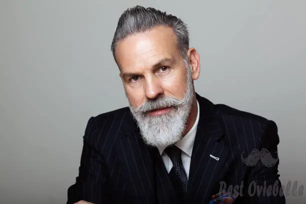 portrait of attractive bearded gentleman wearing trendy suit over empty gray background. studio shot fashion concept. -